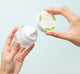 A jar of Mint Condition Hand Renewal Balm made with peptides being opened on a green background