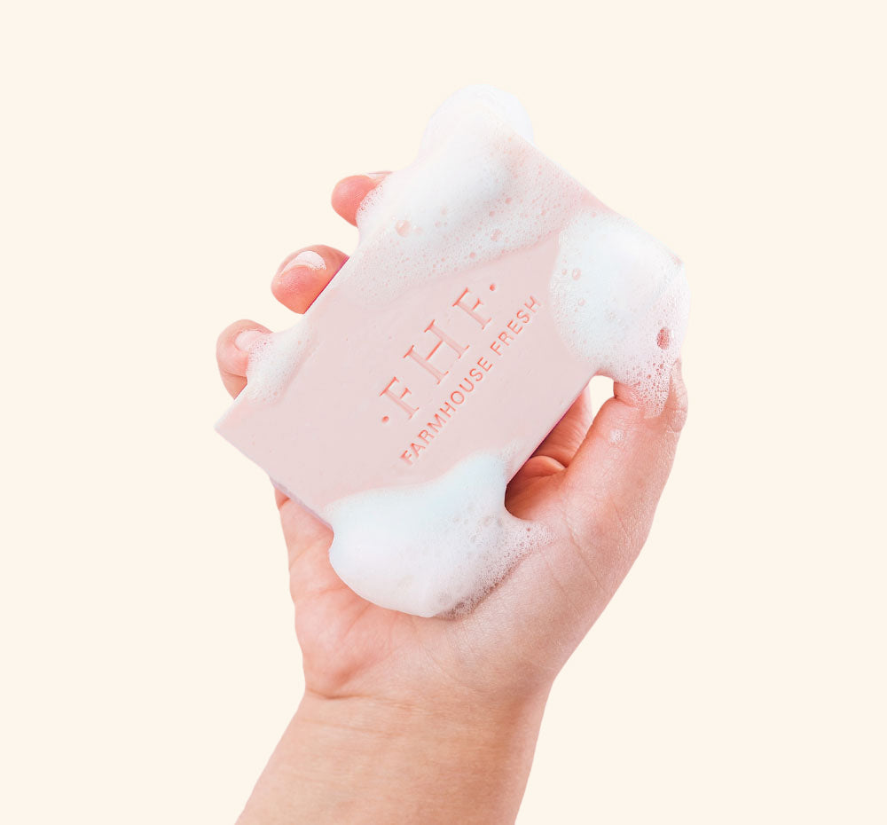 A hand holding a bar of softly scented FarmHouse Fresh Pink Moon Shea Butter Bar Soap with rich lather on it.