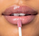 A woman is applying FarmHouse Fresh Vitamin Glaze Lip Gloss in Delicate Rose color that brings color to lips.