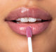 A woman is applying FarmHouse Fresh Vitamin Glaze Lip Gloss in Violet Orchid color that hydrates lips.