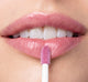 A woman is applying FarmHouse Fresh Vitamin Glaze Lip Gloss in Violet Orchid color that restores dull lips.