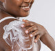 A woman is applying FarmHouse Fresh Ahhhsome Relief Foam-to-Oil After Sun Body Mousse onto her shoulder to soothe sunburnt skin.