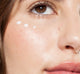 A close up of a woman's face with Farmhouse Fresh Crow Catcher serum applied to her eye area, targeting wrinkles.