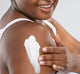 A woman is applying FarmHouse Fresh Harvest Green Shea Butter on her shoulder to hydrate and soften skin.