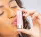 A woman is holding a tube of FarmHouse Fresh Strawberry Mood Fruit Lip balm that nourishes lips with a hint of color.