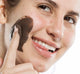 A woman is applying FarmHouse Fresh Sundae Best Chocolate Mask on her face to soften skin and fight wrinkles.