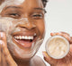 A woman is holding a jar of Farmhouse Fresh Finely Awake cleansing face scrub that exfoliates and brings silky smoothness to skin.