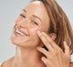 A woman is applying FarmHouse Fresh Flat Out Firm Hyaluronic Acid Peptide Firming Serum onto her faced to instantly firm and renew her complexion.