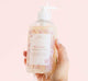 A hand holding a bottle of gentle Pink Moon Body Wash body wash for sensitive skin by Farmhouse Fresh.