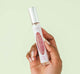 A hand holding all-natural Pink Moon Travel Spray Perfume by FarmHouse Fresh with a soft, delicate scent.