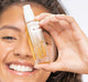 A woman is holding a bottle of FarmHouse Fresh Pretty Amped Renewing and Nourishing Face Oil with CBD that calms skin.