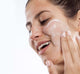 A woman is applying FarmHouse Fresh Pudding Apeel Face Mask on her face to gently exfoliate her sensitive skin without irritation.