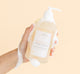 A hand holding a bottle of FarmHouse Fresh Rainbow Road Soothing Body Wash covered with rich suds.