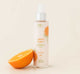 A bottle of FarmHouse Fresh Smooth Reveal Resurfacing Silky Serum that gently exfoliates and visibly smooths the look of rough, bumpy skin texture, next to an orange.
