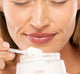 A woman is holding a jar of FarmHouse Fresh Sugar Moon Dip Body Mousse and an applicator wand, enjoying the delicious softly sweet notes of sugar and vanilla.