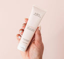 A hand holding a tube of FarmHouse Fresh Sugar Moon Dip Back To Youth Ageless Mousse for Hands scented with soft notes of sweet, sugary vanilla.