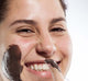 A woman is applying FarmHouse Fresh Sundae Best Chocolate Mask on her face to soften skin and fight wrinkles.