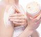 A woman is applying FarmHouse Fresh Sunny Dippin’ Foaming Body scrub onto her shoulder to cleanse and exfoliate skin.