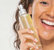 A smiling woman is holding a bottle of Super Lettuce Facial Tonic by Farmhouse Fresh, a natural toner for oily skin.A smiling woman is holding a bottle of Super Lettuce Facial Tonic by Farmhouse Fresh, a natural, alcohol-free toner for oily skin.