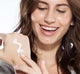 A woman is applying FarmHouse Fresh Sweet Cream Body Milk Lotion on her hand to moisturize and nourish skin.