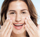A woman is applying FarmHouse Fresh Three Milk Ageless Moisturizer on her face to moisturize and improve the appearance of deep wrinkles.