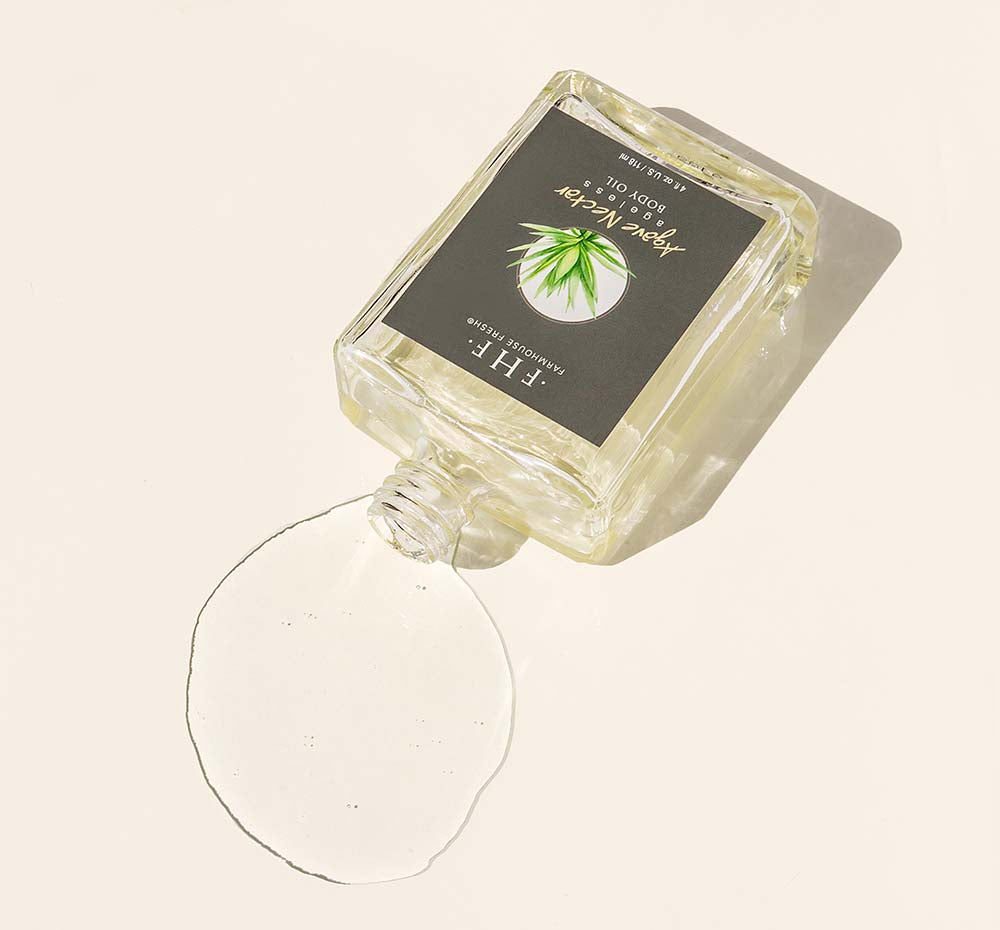 A bottle of FarmHouse Fresh Agave Nectar Ageless Body Oil on its side with oil spilling out of it.