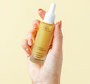 A hand holding a bottle of FarmHouse Fresh Bakuchiol Booster serum that smooths and brightens skin.