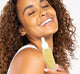 A smiling woman is holding a bottle of FarmHouse Fresh Bakuchiol Booster serum, showing her radiant and refined skin.