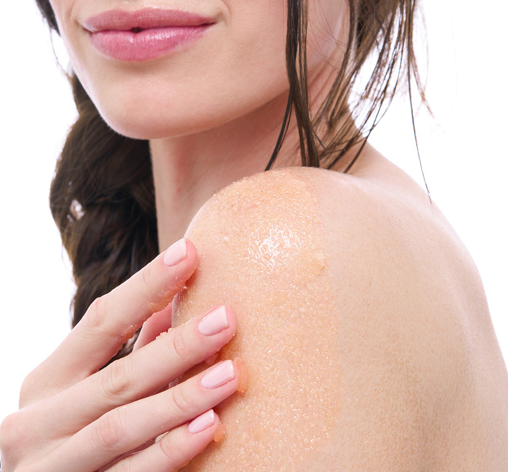 Close-up of a woman applying FHF Blood Orange Glowrita body polish to her shoulder on a white background