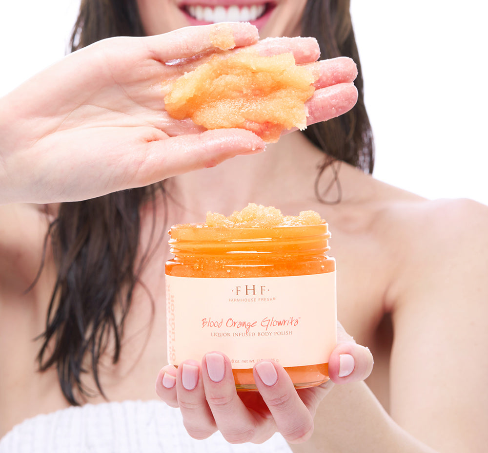 Person holding a jar of FHF Blood Orange Glowrita body polish showing the texture in her hand