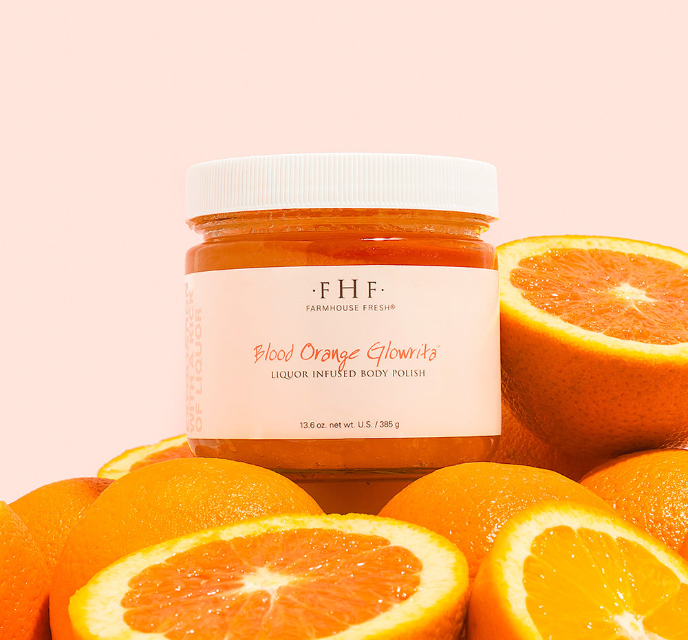 Jar of FHF Blood Orange Glowrita body polish surrounded by oranges on a pink background