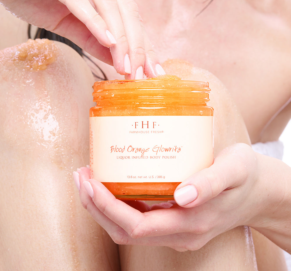 Person holding a jar of FHF Blood Orange Glowrita body polish in front of their legs