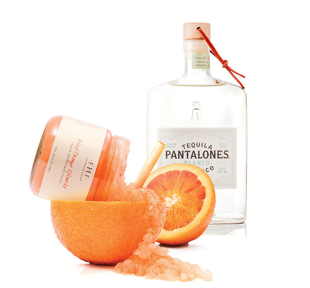 FarmHouse Fresh Blood Orange Glowrita body polish with Pantalones Blanco tequila bottle, orange halves, and scrub crystals