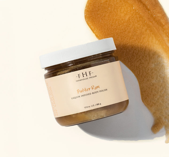 A jar of FHF Butter Rum liquor infused body polish with a white lid against a solid beige background with a texture swipe.