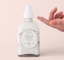 A hand next to a bottle of Buttermilk Lavender Steeped Milk Lotion for body, infused with coconut milk and organic lavender flowers from Farmhouse Fresh.