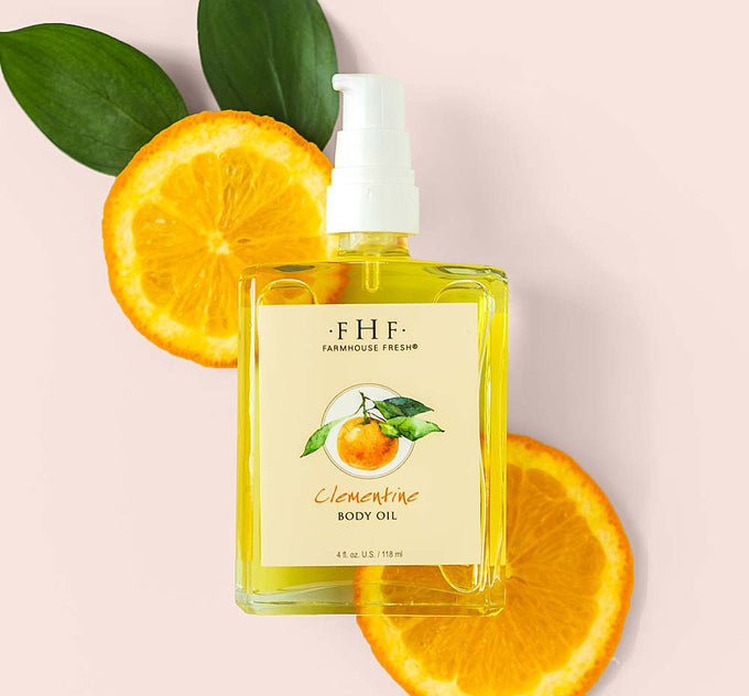 A bottle of light, citrusy Clementine Body Oil by FarmHouse Fresh on top of orange slices.