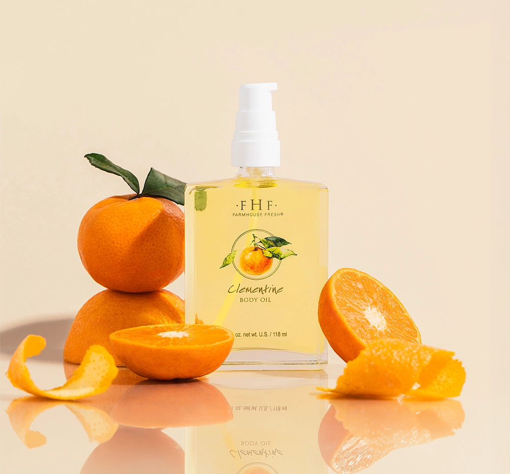 A bottle of light, citrusy Clementine Body Oil by FarmHouse Fresh in front of oranges and orange slices.