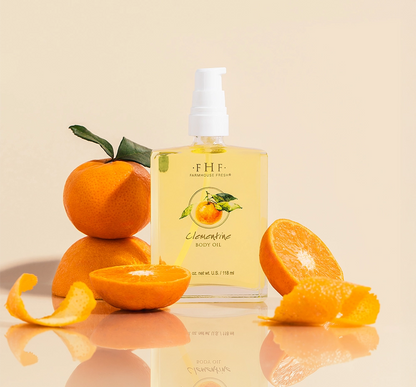 A bottle of light, citrusy Clementine Body Oil by FarmHouse Fresh in front of oranges and orange slices.