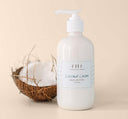 A coconut next to a bottle of Farmhouse Fresh Coconut Cream Shea Butter body lotion that provides nourishment and moisturization for dry skin.