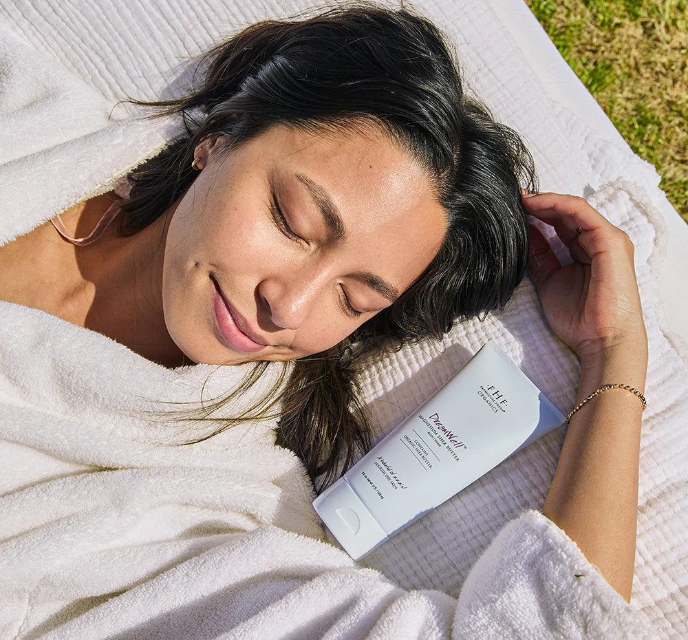 Woman sleeping in a bed on the grass next to DreamWell™ Magnesium Organic Shea Butter Body Cream
