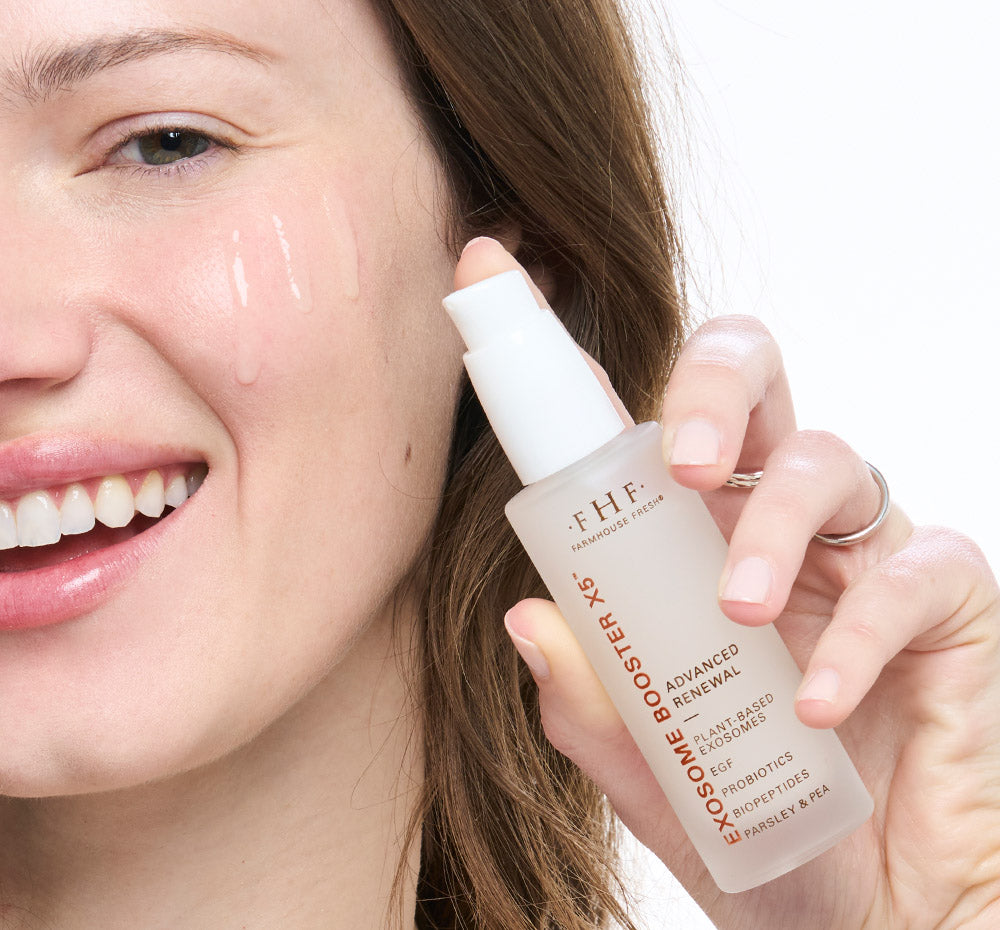 Woman holding FHF Exosome Booster X5 bottle close to her face with product dripping down cheek.