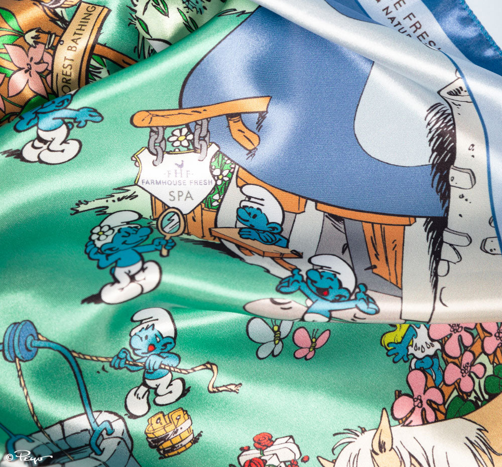 A close-up of FarmHouse Fresh Smurf Village Silky Scarf that can be used to adorn your bag, tie back your hair, or wear around your neck. All profits benefit animal rescue initiatives around the country.