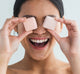 A happy looking woman is holding two Sweet Bath bombs by FarmHouse Fresh in front of her eyes.