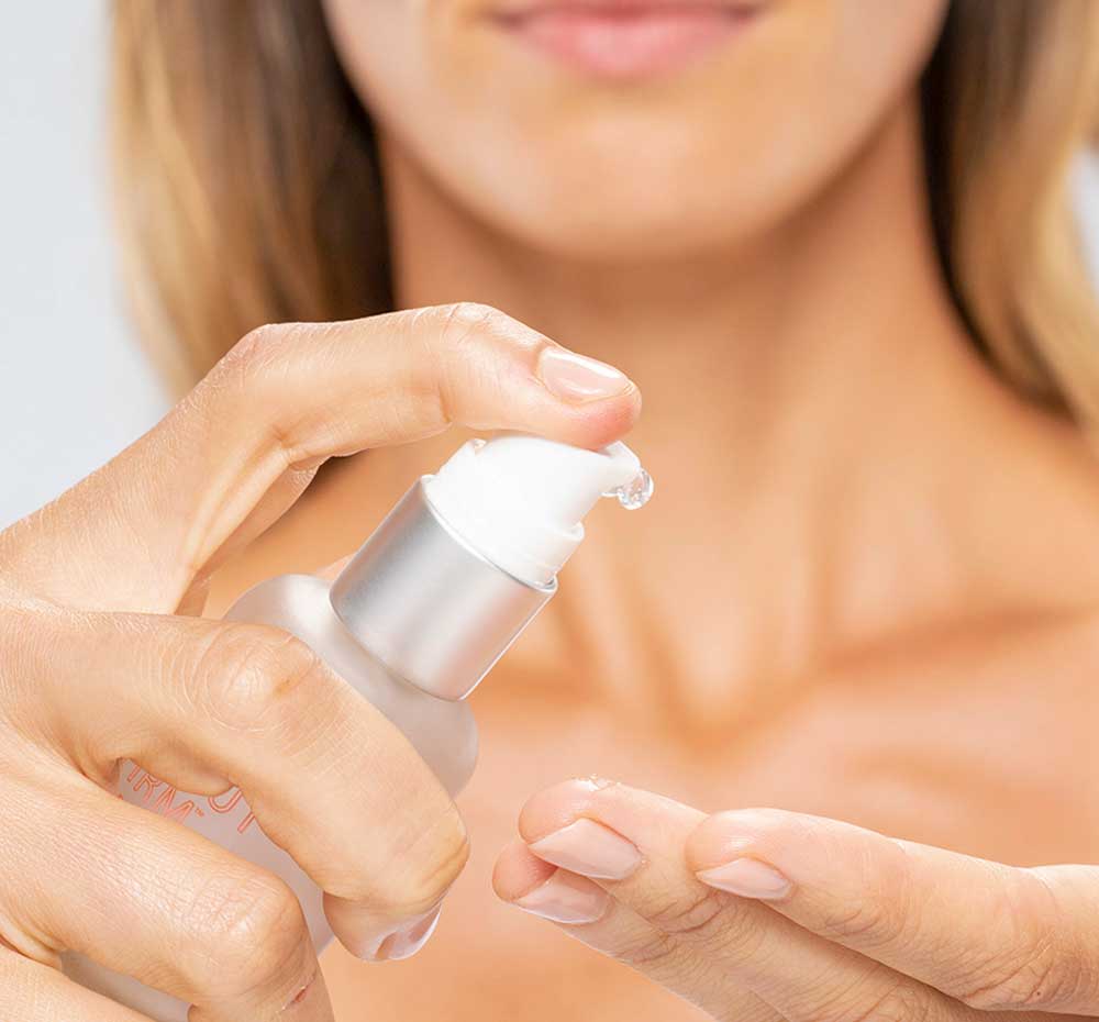 A woman is squeezing a dab of FarmHouse Fresh Flat Out Firm Hyaluronic Acid Peptide Firming Serum on her finger before applying it to her face to smooth the look of wrinkles.