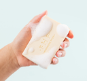 A hand holding a bar of soflty scented FarmHouse Fresh Fluffy Bunny Shea Butter Bar Soap with rich lather on it.