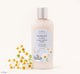 A bottle of FarmHouse Fresh Forest Flower Creamy Chamomile face wash that soothes skin, next to chamomile flowers.