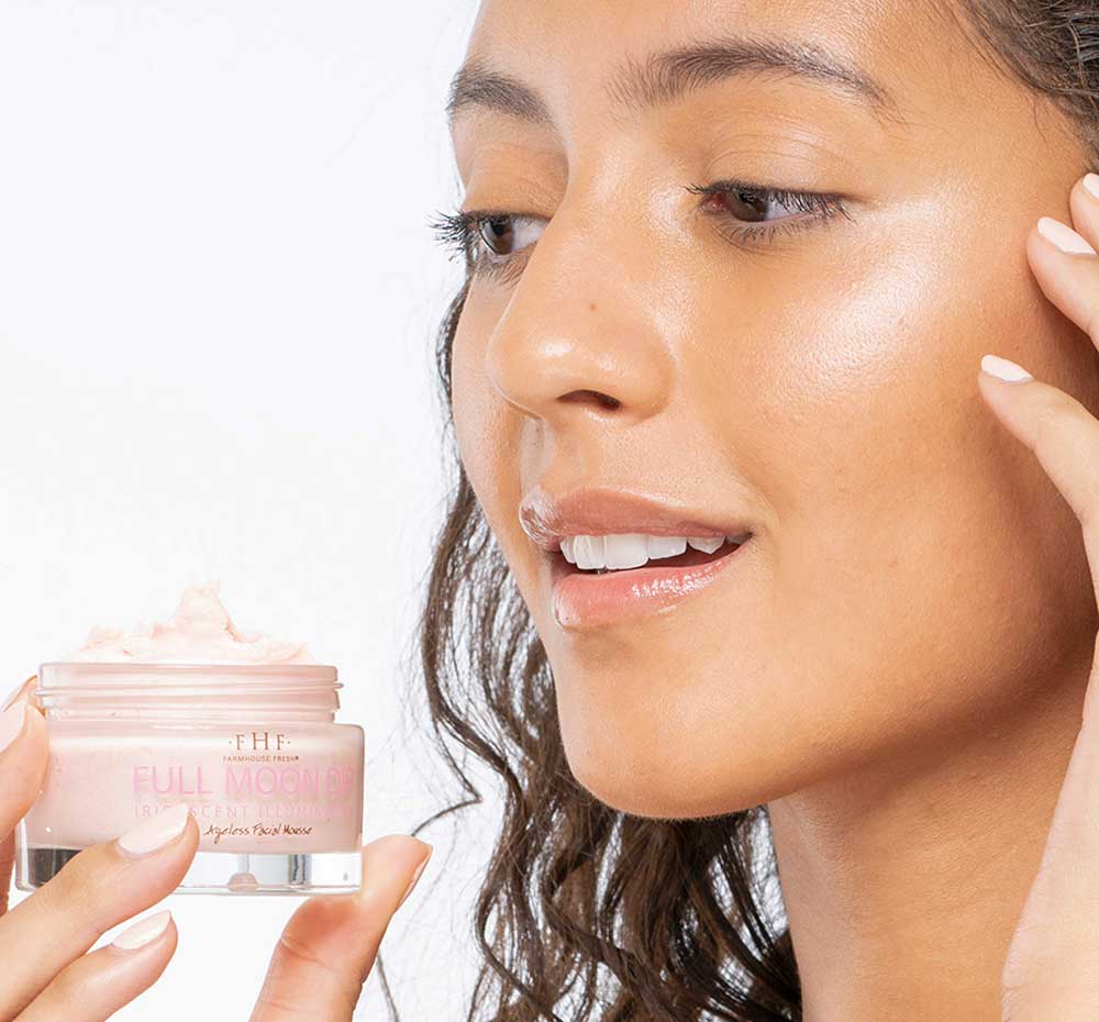 A woman is holding up a jar of Farmhouse Fresh Full Moon Dip with a soft, natural mineral iridescence.