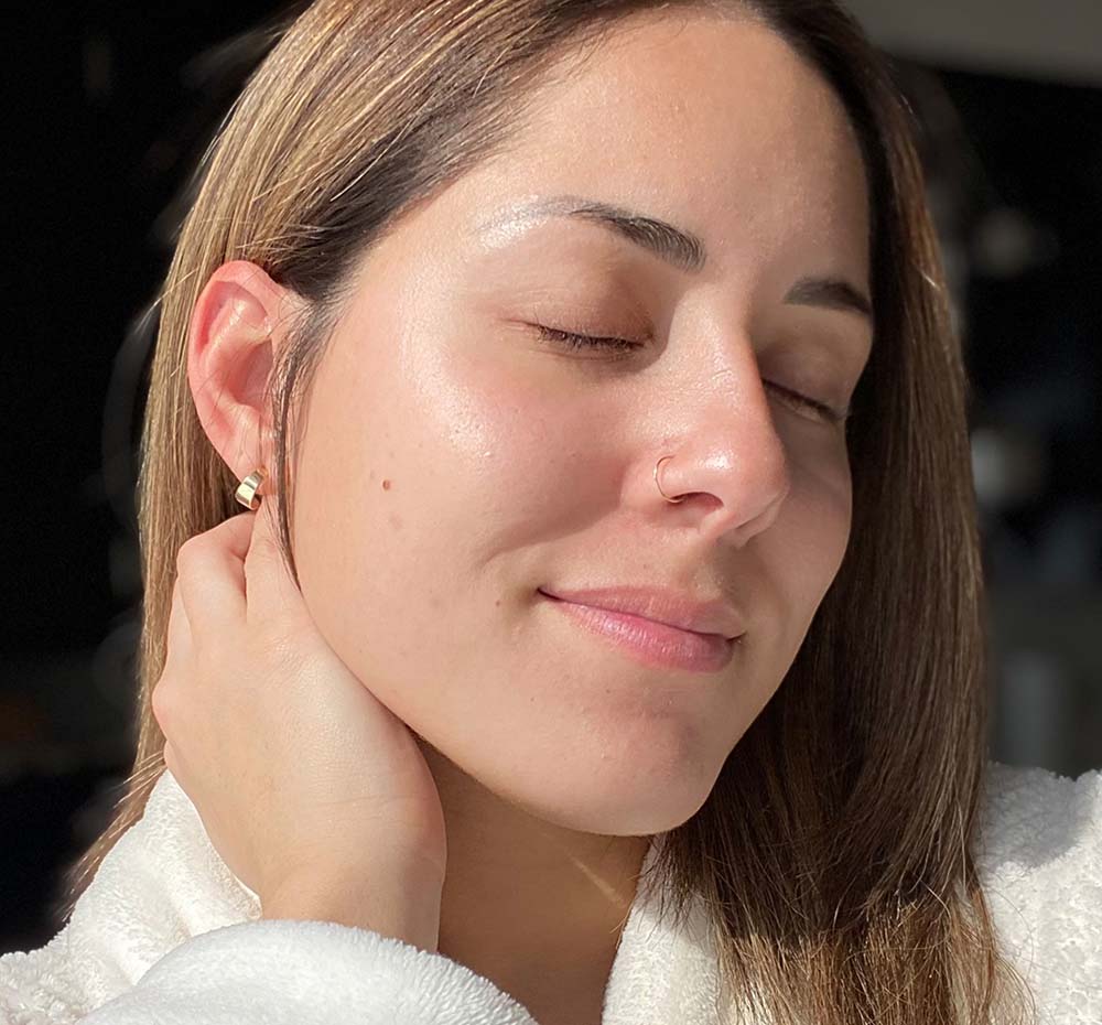 A woman is demonstrating her beautiful, glowing complexion after using FarmHouse Fresh Full Moon Dip Illumination Face Mousse with Retinol and Wrinkle-Targeting Peptides.