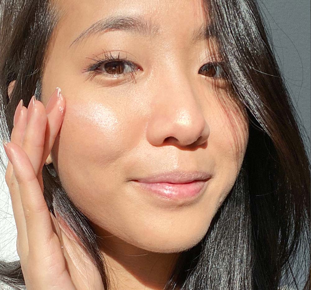 A woman is demonstrating her beautiful, glowing complexion after using FarmHouse Fresh Full Moon Dip Illumination Face Mousse with Retinol and Wrinkle-Targeting Peptides.