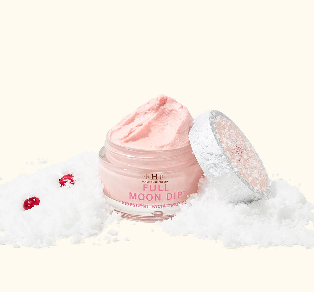 FarmHouse Fresh Full Moon Dip Illumination Mousse body moisturizer styled in snow with festive holiday greenery and red berries